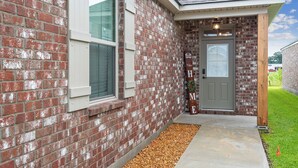 A brick house with a gray door, a welcome sign, and a small porch area. - Minutes from LSU, SU, & Downtown Baton Rouge! (Brusly)