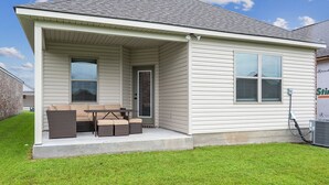 A single-story house with a covered porch, a small patio table, and a cushioned outdoor seating area. - Minutes from LSU, SU, & Downtown Baton Rouge! (Brusly)