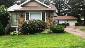 A single-story house with a brick facade, a front door, and a small front yard with a bush and a lawn. - The Gathering Place, rent the entire home (Erie)