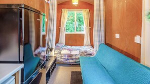 Een smalle kamer met houten wanden, een bed met behang en een blauwe bank, en een koelkast.