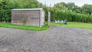 Een houten tuinhuisje met een grindpad en een picknicktafel met stoelen.