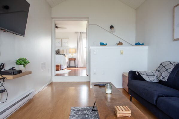 Ein modernes Wohnzimmer mit Flachbildfernseher, Holzboden, einer dunkelgrauen Couch und einer Treppe, die in einen anderen Raum führt.
