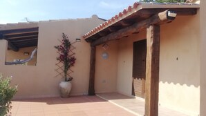 A covered outdoor area with a tiled floor, a wooden pergola, a potted plant, and a door. - DomusParadiso (Costa Paradiso)