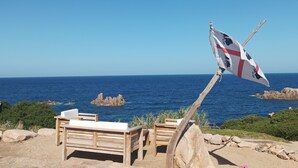 A beach with wooden benches and a flagpole with a flag. - DomusParadiso (Costa Paradiso)