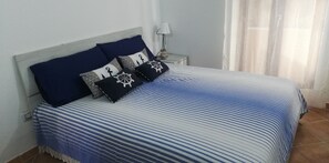 Una cama con una colcha azul y blanca a rayas, almohadas añil con motivos náuticos y una mesita de noche con una lámpara.