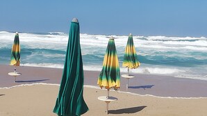 Beach umbrellas on a sandy beach with waves in the background. - DomusParadiso (Costa Paradiso)