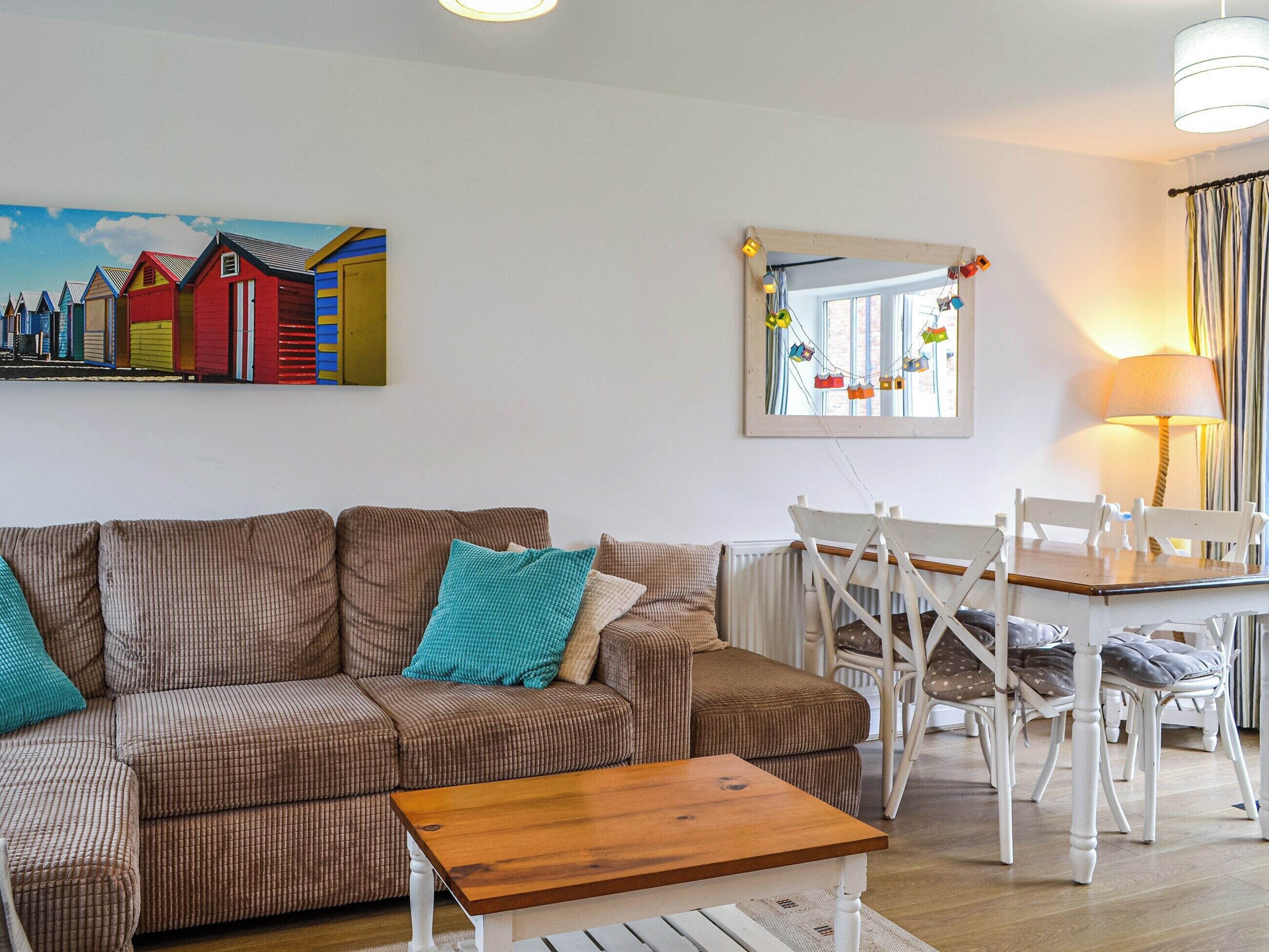 Un salón acogedor con un sofá marrón, una mesa de centro de madera y una zona de comedor con sillas blancas y una mesa.