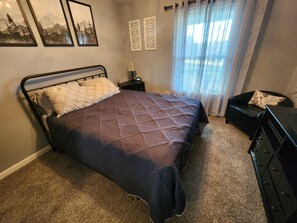 A bedroom with a bed, a nightstand, a dresser, a chair, and a window with curtains.