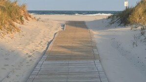 Un paseo marítimo de madera que conduce a la playa, bordeado por dunas de arena y una vista despejada del océano.