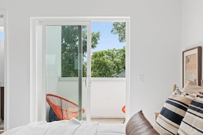 A room with a bed, a chair, and a sliding glass door leading to an outdoor area with a view of trees and a house. - South Side Modern | DT Chattanooga| A+ Walkable (Chattanooga)