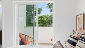 A bedroom with a bed, a chair, and a sliding glass door leading to a balcony with a view of trees and a house. - South Side Modern | Downtown Living | A+ Location., South Side Modern | Downtown Living | A+ Locatio (Chattanooga)