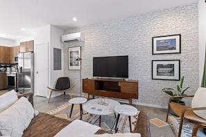A modern living room with a brick wall, a flat-screen TV, and a dining area with a round table. - South Side Modern | DT Chattanooga| A+ Walkable (Chattanooga)