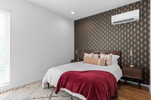 A bedroom with a bed, nightstands, an air conditioning unit, and a patterned wall. - South Side Modern | DT Chattanooga| A+ Walkable (Chattanooga)