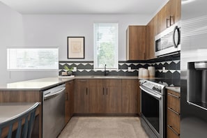 A modern kitchen with wooden cabinets, stainless steel appliances, a black and white backsplash, and a window with blinds. - South Side Modern | DT Chattanooga| A+ Walkable (Chattanooga)