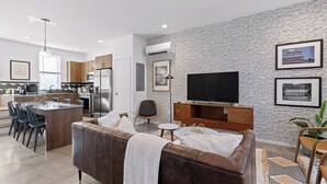 A modern living room with a brown leather sofa, a dining area with chairs, a kitchen with stainless steel appliances, and a wall with a newspaper print design. - South Side Modern | Downtown Living | A+ Location., South Side Modern | Downtown Living | A+ Locatio (Chattanooga)