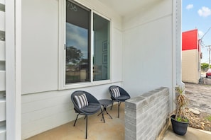 Fachada residencial blanca, una ventana con el número 738, dos sillas exteriores y una planta en maceta.
