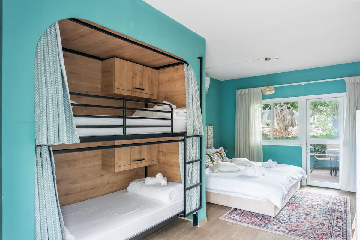 Ein Zimmer mit einem Etagenbett, einem Einzelbett und einem großen Fenster mit Blick auf Grünflächen.