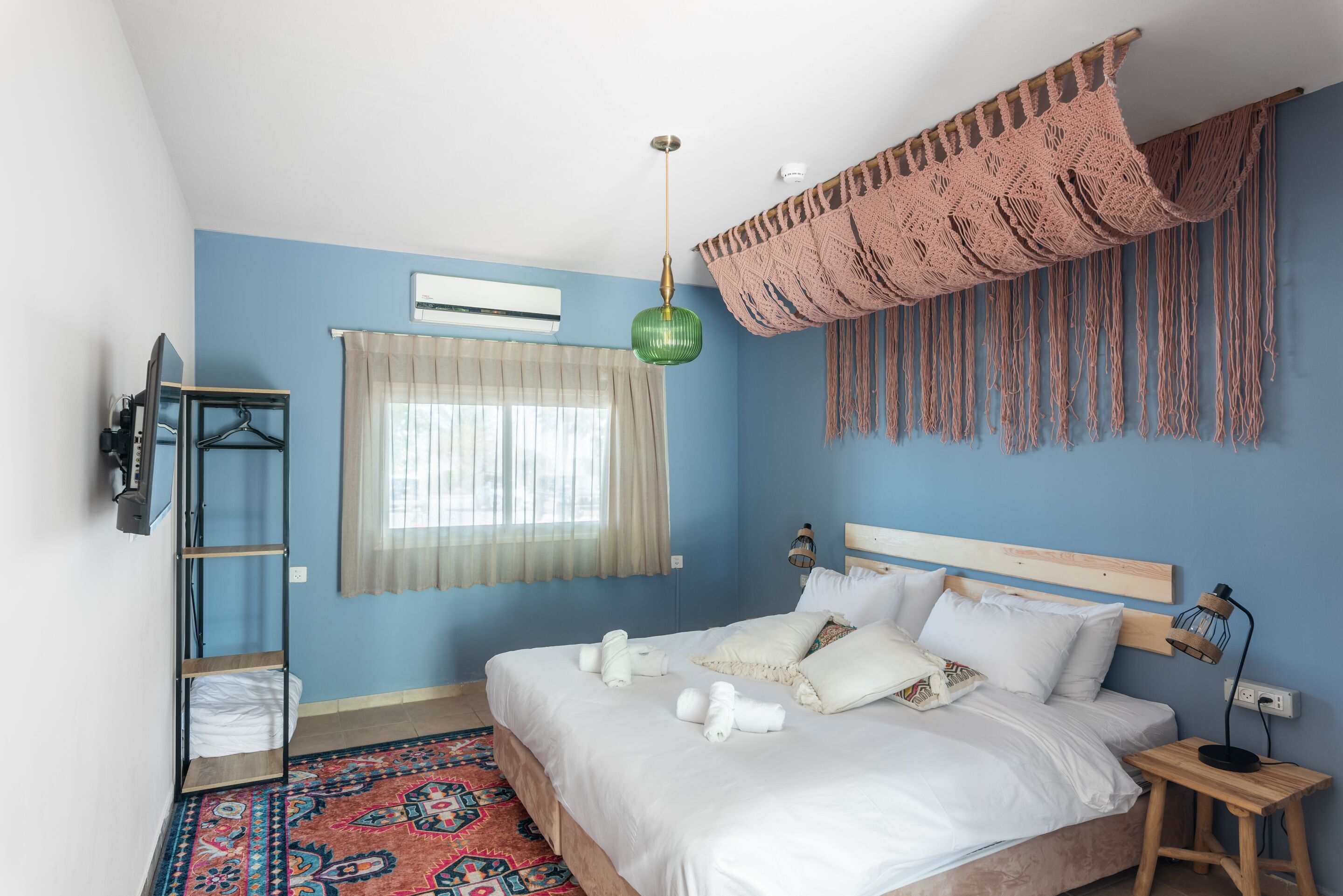 A bedroom with a bed, a hanging light, a TV, and a window with curtains.
