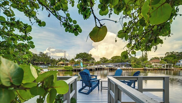 A wooden dock with blue chairs and a table, overlooking a calm body of water with houses in the background. - Pet-Friendly Waterfront Home - 2 Mi to Beach! (Tarpon Springs)
