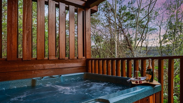 A wooden deck with a hot tub, surrounded by trees and a wooden railing.