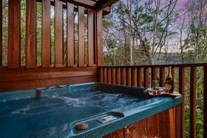 Une terrasse en bois avec un jacuzzi, entourée d’arbres et dotée d’une rambarde en bois.