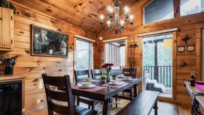 A wooden cabin interior with a dining table set for four, a chandelier, and a framed picture of bears on the wall.