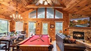 A wooden cabin interior with a pool table, dining area, and fireplace.