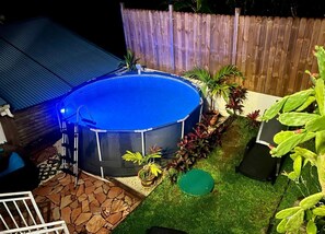 A circular swimming pool with a blue cover, surrounded by a wooden fence, potted plants, and a stone patio. - Villa Iguana, peaceful duplex, magnificent view of the sea and Diamond Rock, swimming pool (Sainte-Luce)