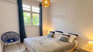 Une chambre à coucher avec un lit, une chaise, une table de chevet et une fenêtre avec des rideaux.