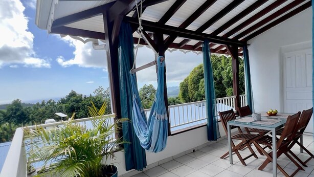 Un balcon avec une table et des chaises, un hamac suspendu et une plante en pot.