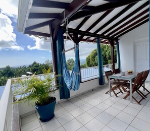 A balcony with a table and chairs, a hanging hammock, and a potted plant. - Villa Iguana, peaceful duplex, magnificent view of the sea and Diamond Rock, swimming pool (Sainte-Luce)
