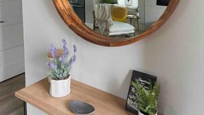 A mirror with a wooden frame on a wall, a small wooden table with a potted plant and a framed picture, and a glimpse of a kitchen and living area in the reflection. - Riverstone Village Pet Friendly Beach Cruisers Sleeps 6 (Coeur d'Alene)