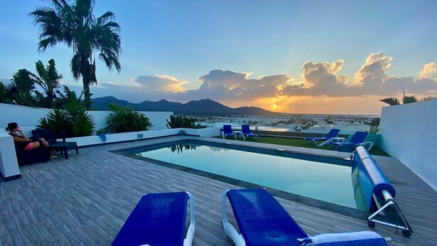 A rooftop pool area with lounge chairs and a view of the sunset over a body of water and mountains. - Luxury villa - with a heated pool, hot tub, sea views, aircon, WiFi, UK TV (Playa Blanca)