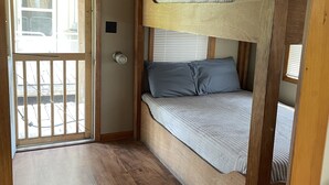 Une chambre avec un lit superposé, un plafond en bois, une porte donnant sur l’extérieur et une fenêtre avec des stores.