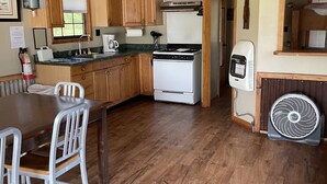 Une cuisine avec des meubles de rangement en bois, une cuisinière, un ventilateur et une table à manger avec des chaises.