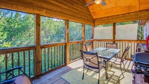 Une terrasse en bois avec une table et des chaises en verre, un ventilateur de plafond et un barbecue.