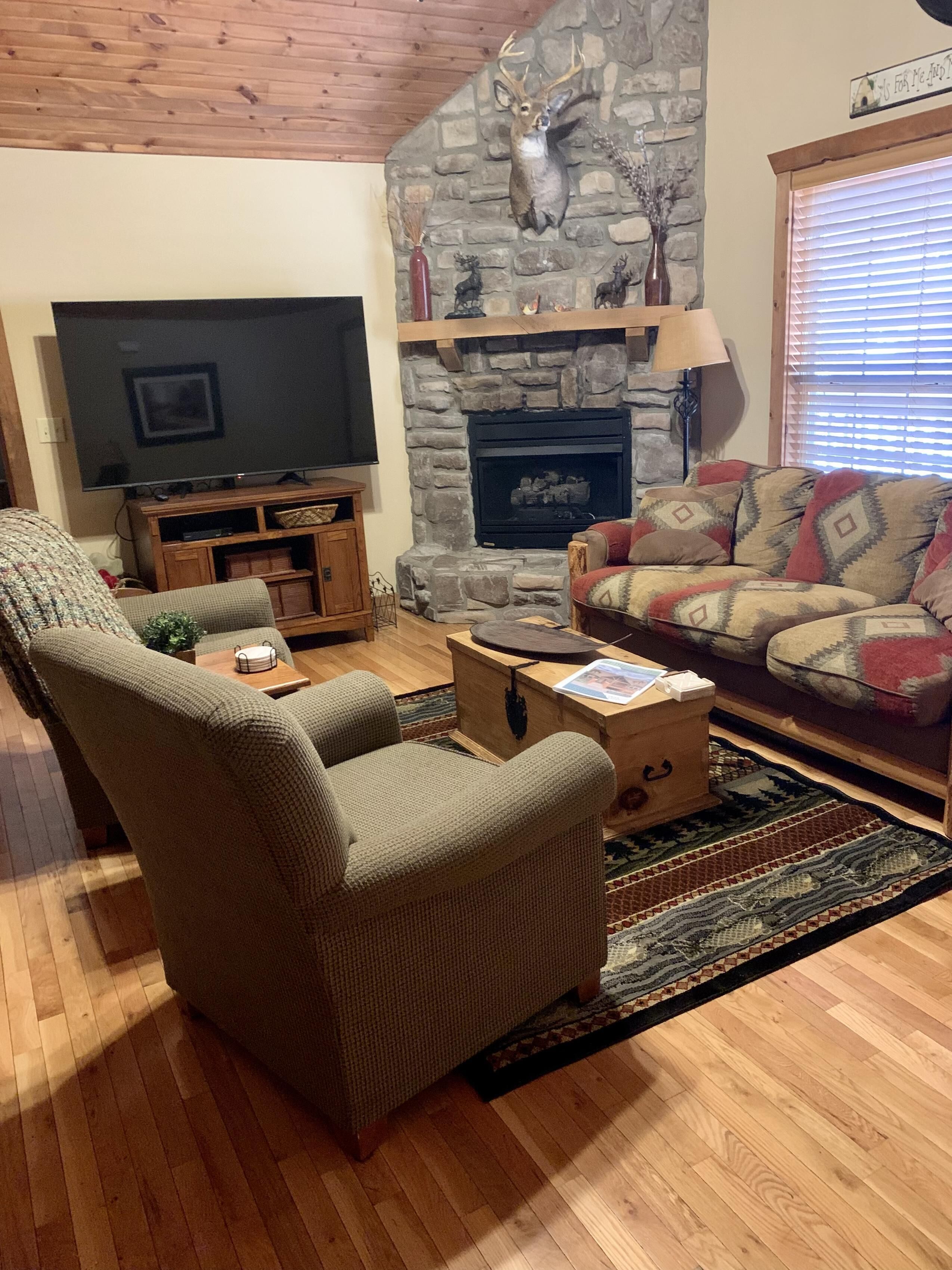 Un salon chaleureux avec une cheminée en pierre, un téléviseur et des fauteuils confortables.