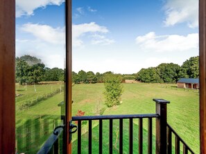 A view from a window overlooking a grassy field with trees and a small building in the distance. - Cosy Country Lodge - UK40802 (High Halden, near Tenterden)
