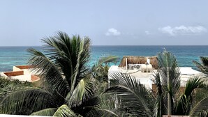 A beachfront property with a thatched-roof structure, palm trees, and a view of the ocean. - Beautiful apartment with balcony, pool, Roof Top in Punta Sur at Casa Ama 2 (Isla Mujeres)