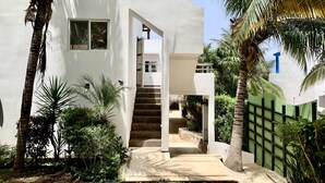 A modern white building with a staircase leading to a covered entrance, surrounded by palm trees and greenery. - Gorgeous cozy apartment with pool, balcony and roof top in Punta Sur! Casa Ama 4 (Isla Mujeres)