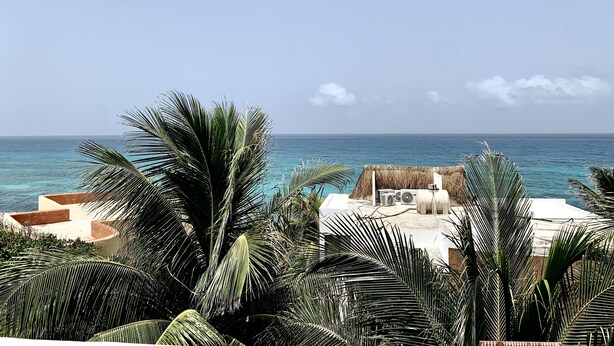 A beachfront property with a thatched-roof structure, palm trees, and a view of the ocean. - Gorgeous cozy apartment with pool, balcony and roof top in Punta Sur! Casa Ama 4 (Isla Mujeres)