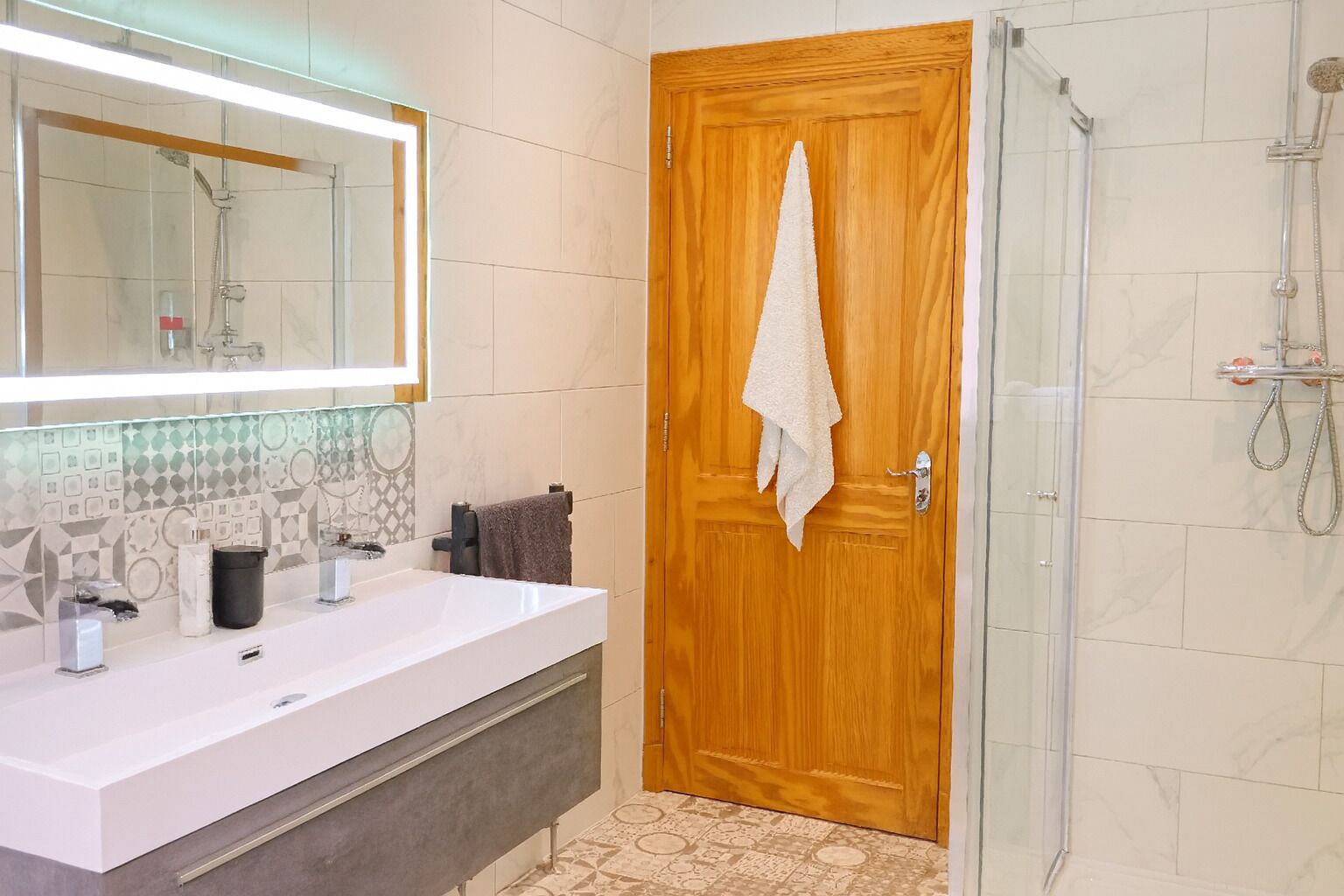 A bathroom with a wooden door, a white sink, a glass shower enclosure, and a tiled backsplash.