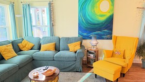 A living room with a sectional sofa, a yellow armchair, a coffee table, a painting, and a lamp. - Casa del Sole • Downtown • 3 Ensuites • Pets OK (Pensacola)