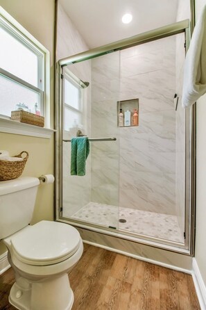 Ein Badezimmer mit einer Duschkabine, einer Toilette, einem Fenster und einem Ablagefach mit Pflegeprodukten.