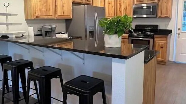 A modern kitchen with wooden cabinets, a central island with stools, stainless steel appliances, and pendant lighting.