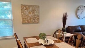 A dining area with a wooden table, chairs, a clock, and a wall art piece.