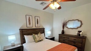 A bedroom with a bed, nightstands, a dresser, a ceiling fan, and wall art.