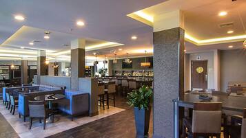 Un hall d’hôtel moderne comprenant un bar, des espaces de détente et un comptoir d’accueil.