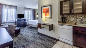 A hotel room with a bed, a desk, a TV, a lamp, a coffee maker, and a kitchen area with a dishwasher and cabinets. - Studio | Free Breakfast, Indoor Pool & Hot Tub (Davenport)