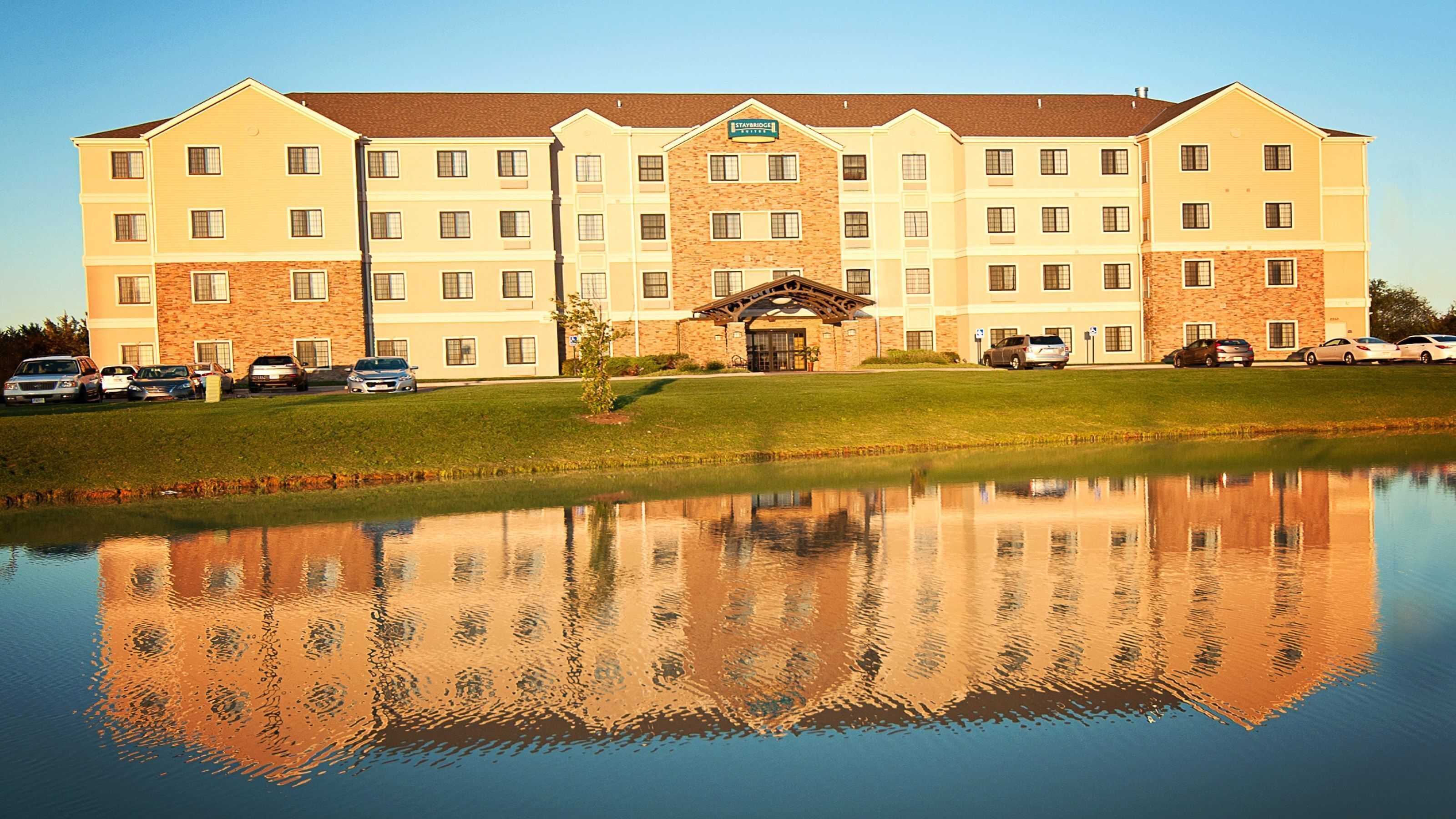 Exterior view at dusk with pond reflection and parking — the hotel is lit and staffed for late arrivals